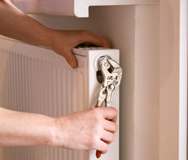 plumber fixing a radiator with pliers on a construction site