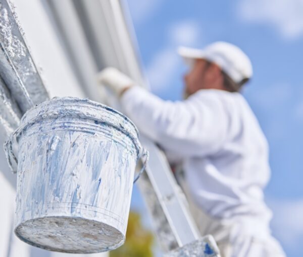 A person in white is painting the exterior of a house using a ladder and a bucket on the roof, in a close-up view. --ar 1:1 --profile hkenas3 --v 7 Job ID: 6293bf11-b692-48dc-bdb0-199437ff9c50