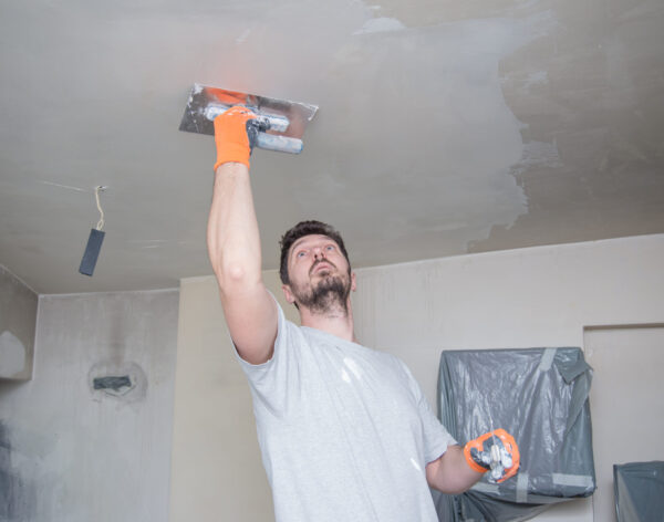 A worker with protective gloves is plastering the ceiling.
