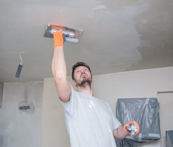 A worker with protective gloves is plastering the ceiling.