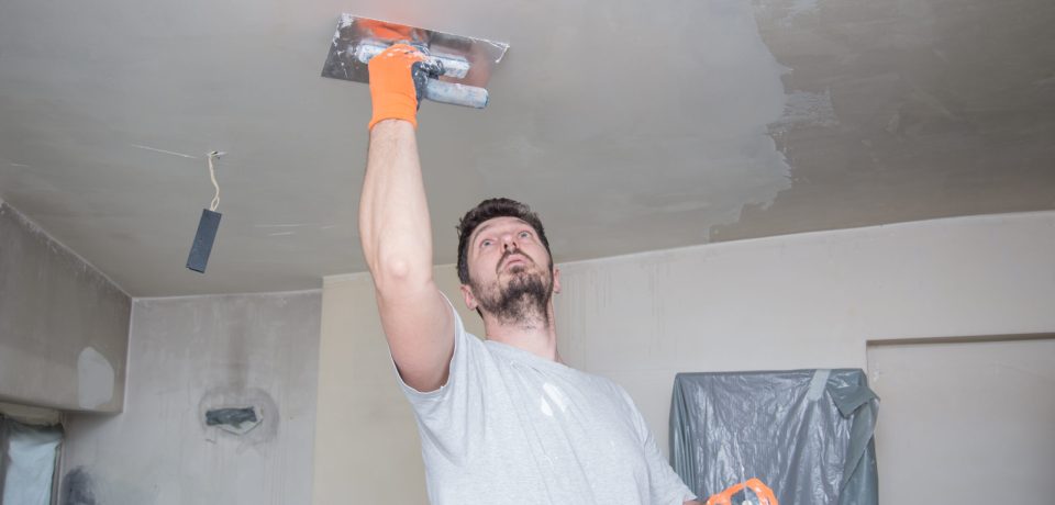 A worker with protective gloves is plastering the ceiling.